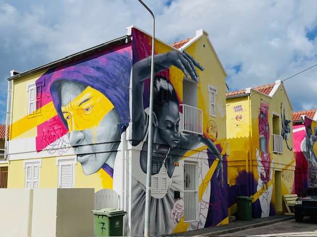 Two prominent yellow buildings with street artwork of ballerina and other figures in Curacao